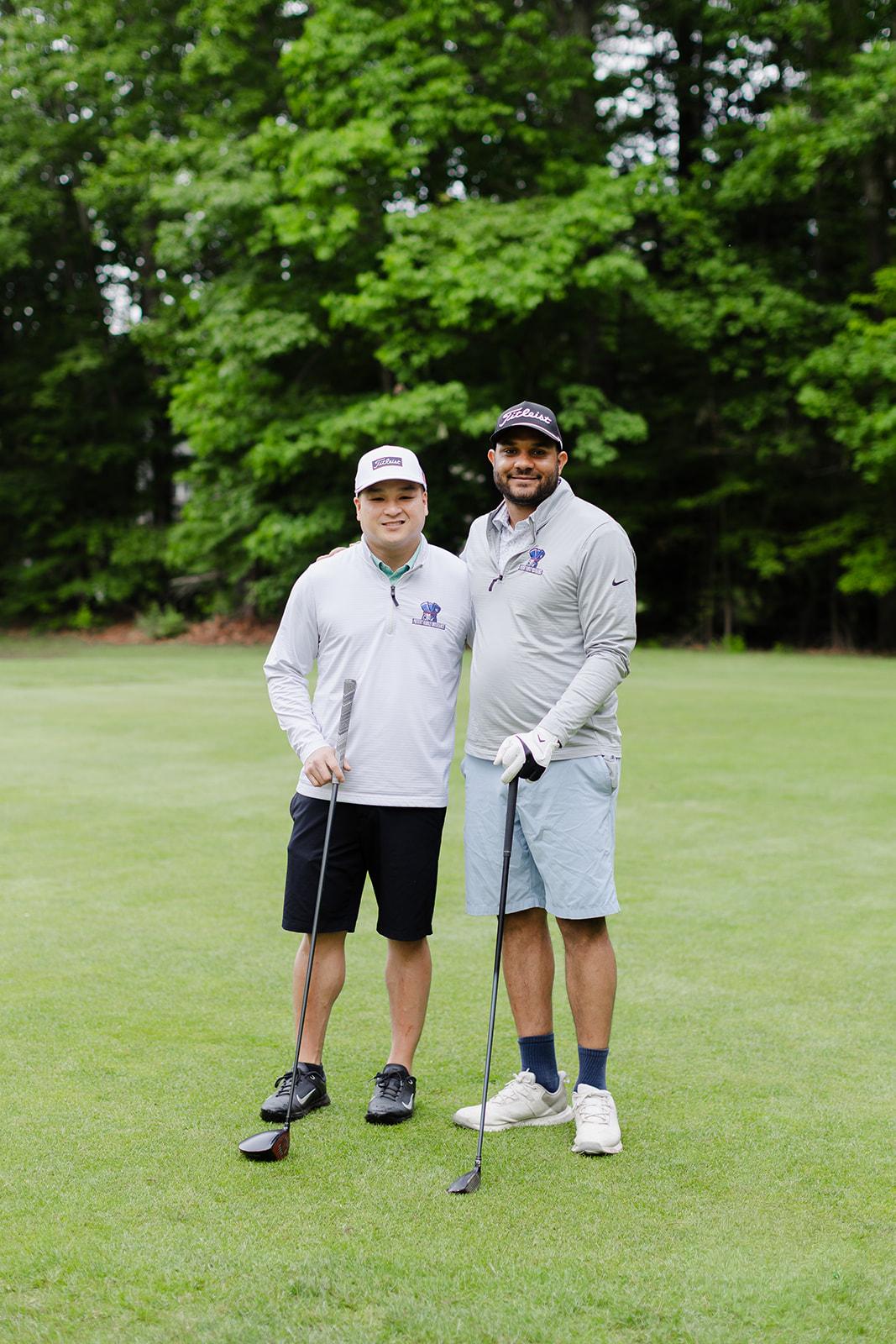 Two Patriot team members in matching grey quarter-zips posing with their clubs